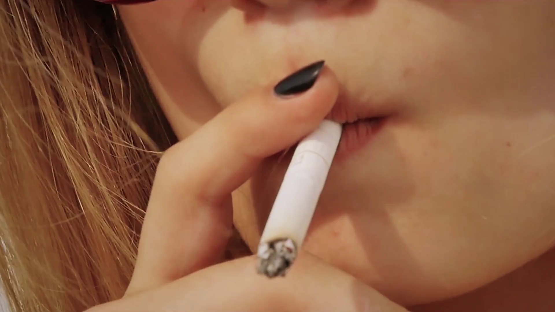 video of smoking cigarettes the girl smokes a cigarette closeup. smoking beautiful woman cigarette  closeup. Front view face closeup holding a cigarette in lips
