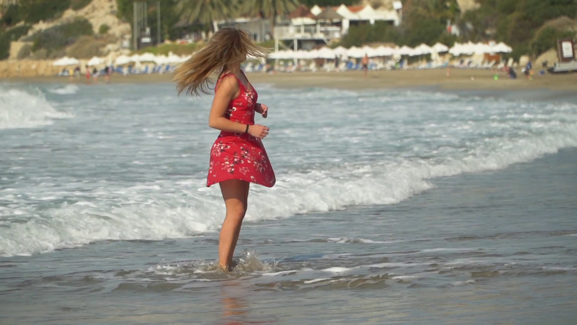 Young woman in red dress spinning by the sea. Enjoying leisure time.