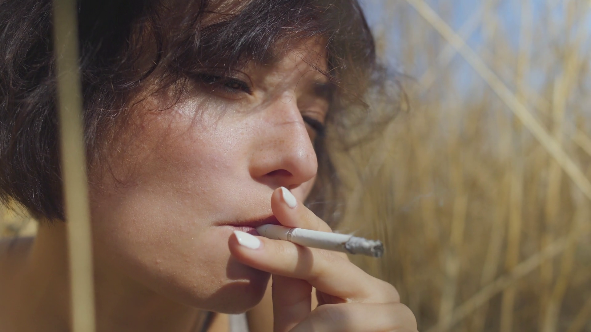 Close-up portrait of chic woman with short hair smoking cigarette sitting  among the wheat field looking away. Confident carefree girl outdoors. Real  people series