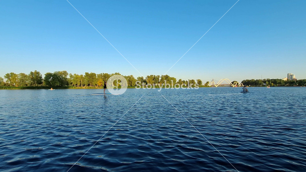 KYIV, UKRAINE, AUGUST 30, 2025: People floating on SUP boards on the Dnieper River in Kyiv city, near Obolonsky Island and Wave Bridge. Stand Up Paddleboard. Video footage from yacht moving in wind