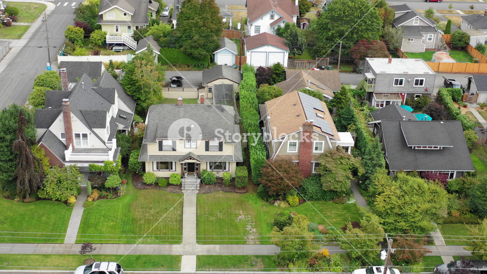 Aerial view of a Pacific Northwest suburban neighborhood shifts downward to show a rooftop with solar panels,; the view expands to give more area context