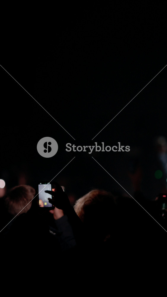 Silhouettes of a crowd at a live music concert. Fans hold up phones to record the show. The stage is lit with dramatic red lights, creating