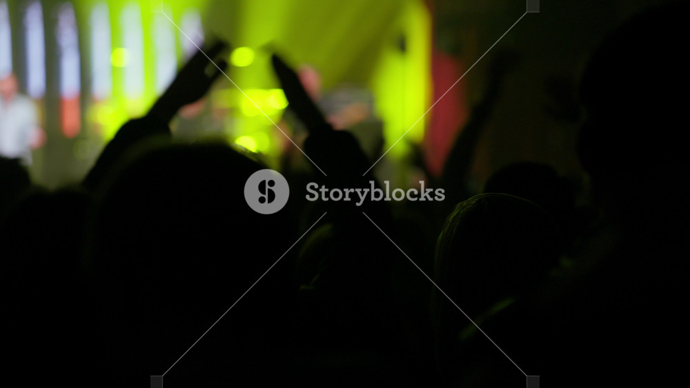 Dynamic video of a silhouetted audience at a lively concert or music festival, raising hands and cheering to vibrant, changing stage lights