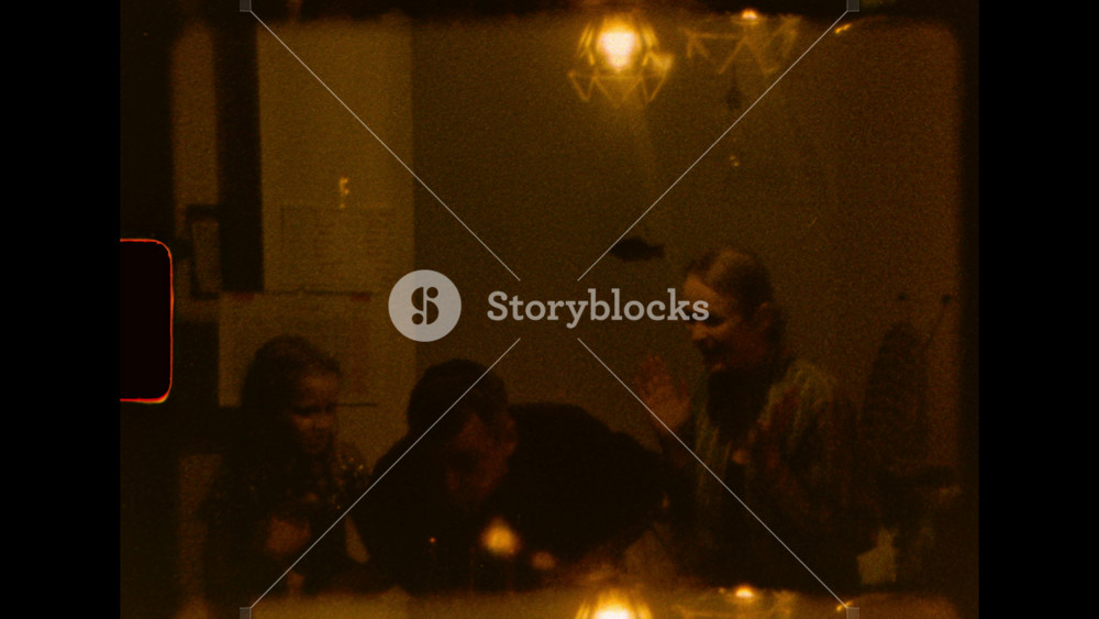 A happy family of three smiles around a table with lit birthday candles under warm lamps on super 8 film scan