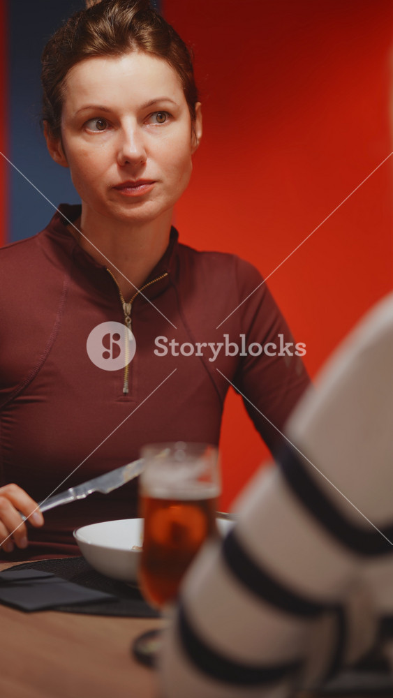 Close up of brunette woman in burgundy zip top holding a red wine glass and speaking expressively, beer glass and bowl visible in foreground