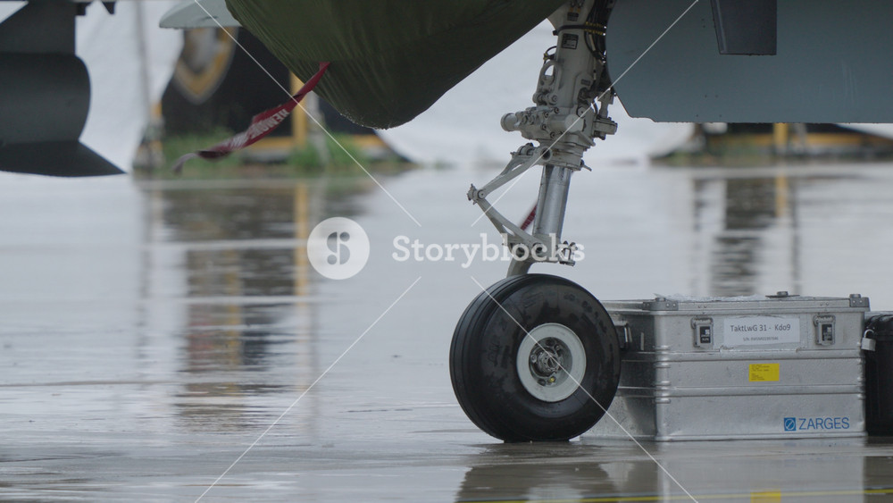 LUQA, MALTA - SEPTEMBER 28, 2025: The landing gear of a military fighter jet stands on a rain soaked apron next to a metal equipment case