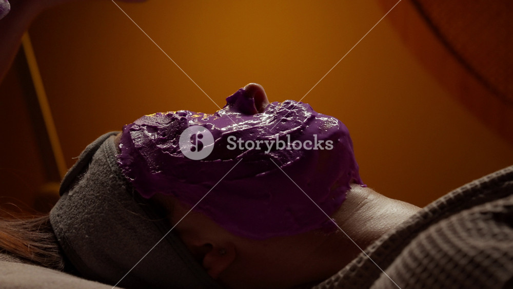 Relaxing spa facial treatment with thick purple face mask applied for skincare, rejuvenation, and soothing wellness on a resting person in