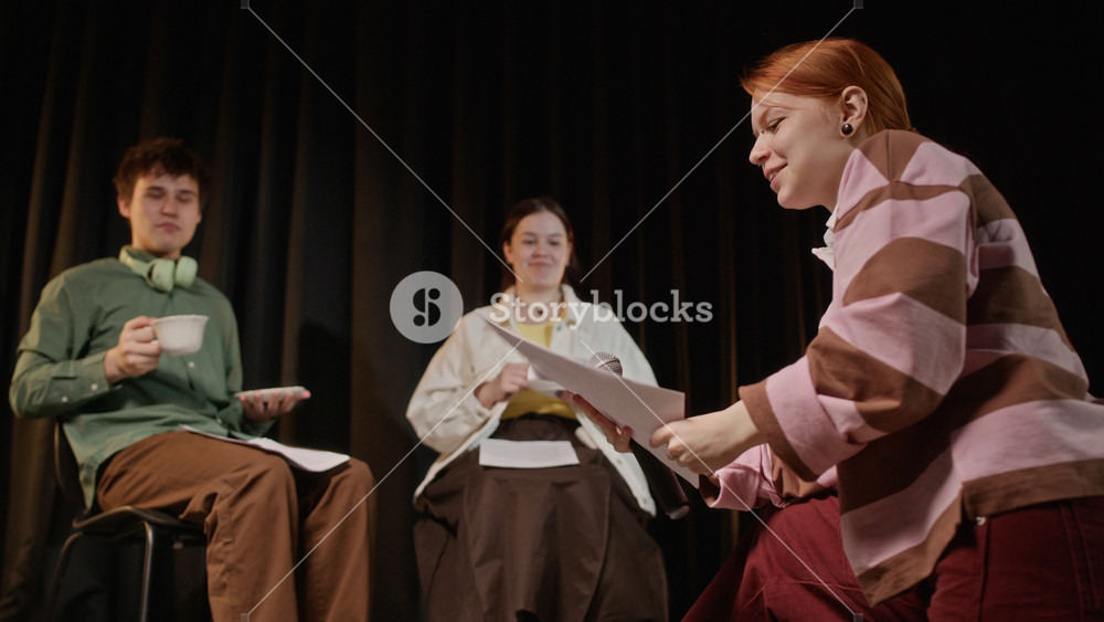 Low angle shot of Caucasian teenagers rehearsing theatrical play on stage with scripts and teacups. Footage for promoting high school drama clubs, youth theater programs, and creative arts education