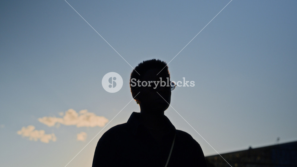 African American young adult woman walking outdoors and looking around against blue sky. Silhouette shot ideal for diversity marketing, urban lifestyle branding, and modern fashion commercials
