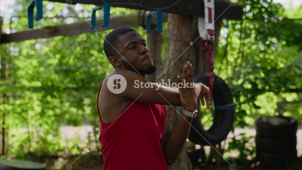African American young adult man stretching arms at outdoor gym, preparing for workout. Ideal for sports apparel advertisements, wellness blogs, and fitness marketing