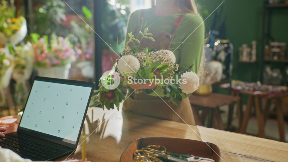 Young adult Caucasian female florist arranging flower bouquet while talking to colleague at counter. Ideal for small business marketing and local retail service promotion