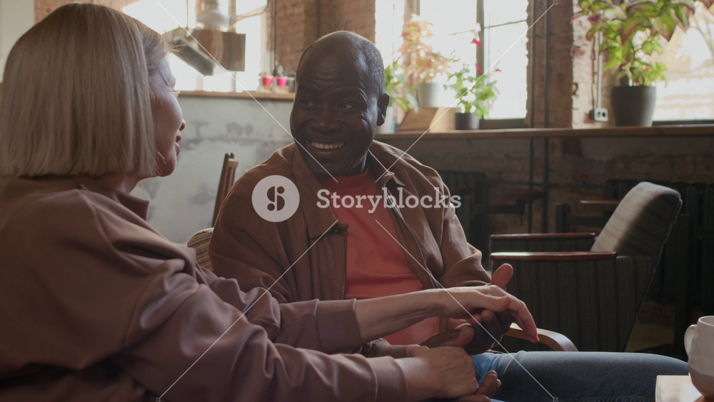 Two adult interracial people in love sharing warm and cheerful interaction in cozy cafe, surrounded by exposed brick walls, mid-century furniture, and natural light
