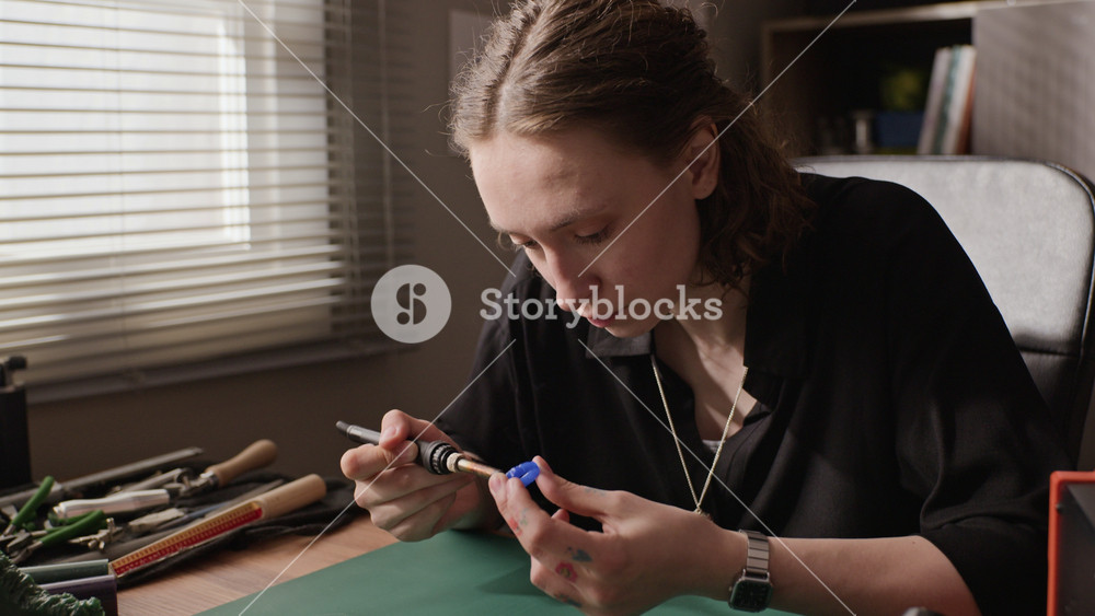 Dolly in shot of Caucasian young adult woman jeweler carving blue wax ring mold with electric pen tool at workshop desk. Clip ideal for promoting handmade jewelry brands or creative small businesses
