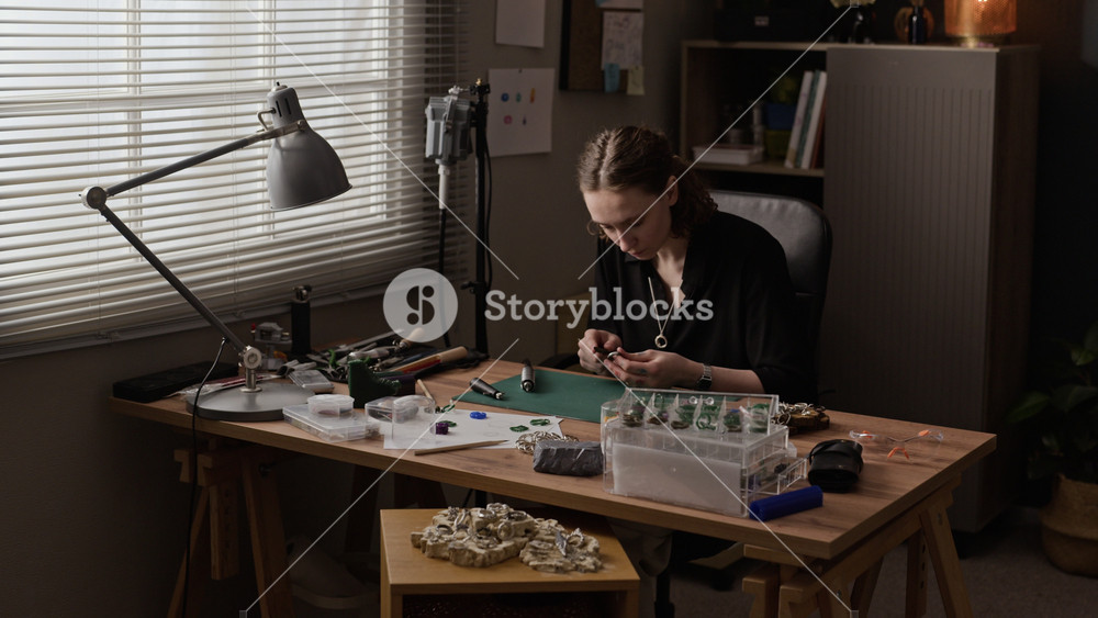 Dolly out shot of Caucasian young woman sitting at workshop desk, crafting handmade jewelry with specialized tools. For promoting small businesses, artisanal crafts, creative entrepreneurship