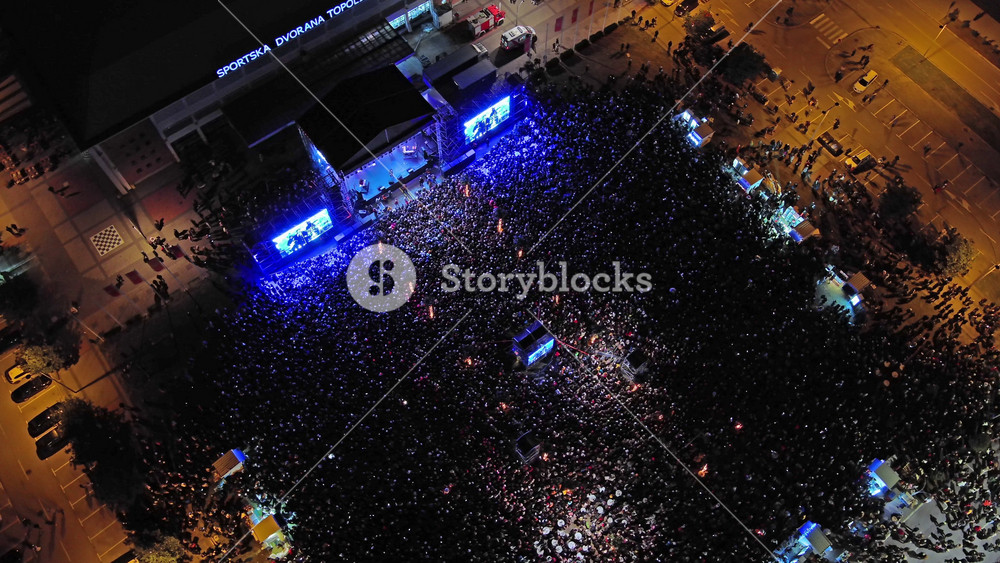 , BAR - JANUARY 01, 2026: Aerial around view of crowd at night music concert. People at outdoor stage with lights and screens, 4k