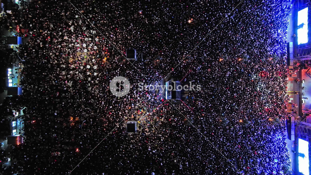Aerial top view of crowd at night music concert. People gathered at festival outdoor stage with lights and screens, 4k