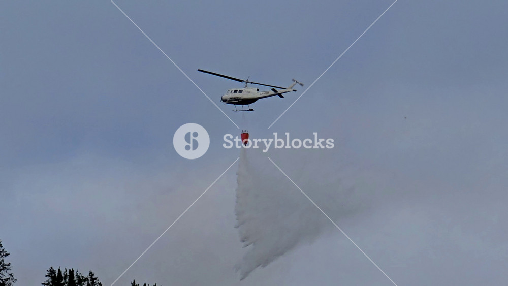 A helicopter works to combat a wildfire in the breathtaking landscapes of Norway. The aircraft hovers above thick forest, releasing water to