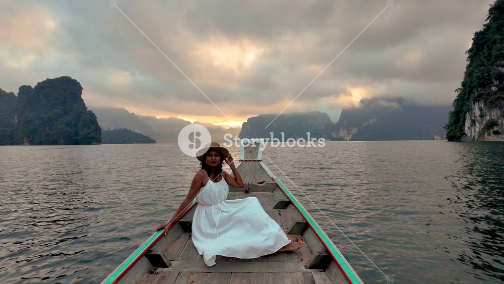 Experience the tranquility of Khao Sok National Park at dawn. A woman in a flowing white dress relaxes on a traditional boat, surrounded by
