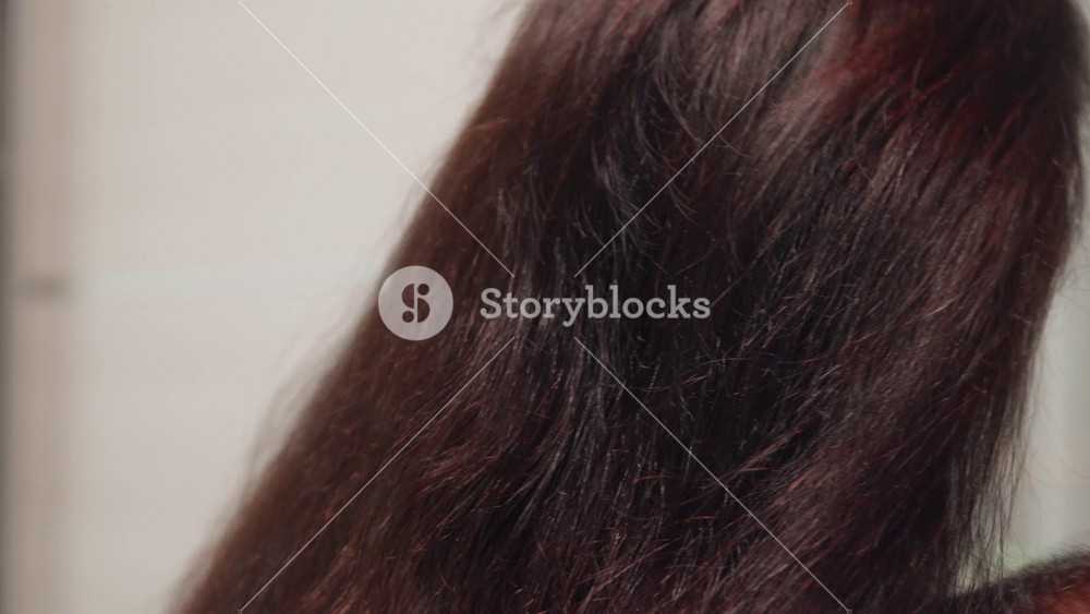 Extreme close up of person brushing smooth dark brown hair with beige plastic comb showing hair texture and strands. Beauty and haircare