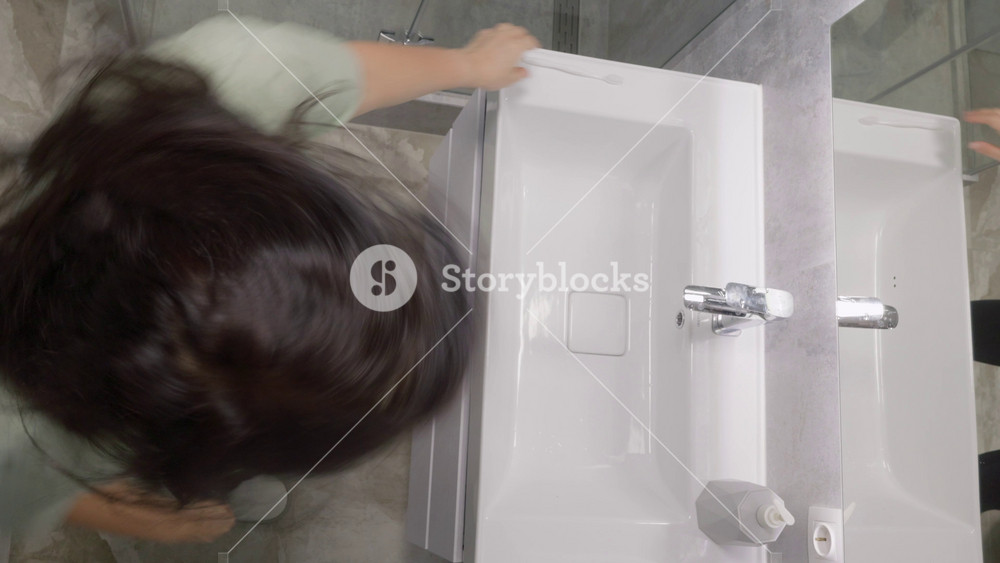 Overhead view of woman wearing mint green short sleeve t-shirt and black leggings dancing at white sink with chrome faucet in modern bright