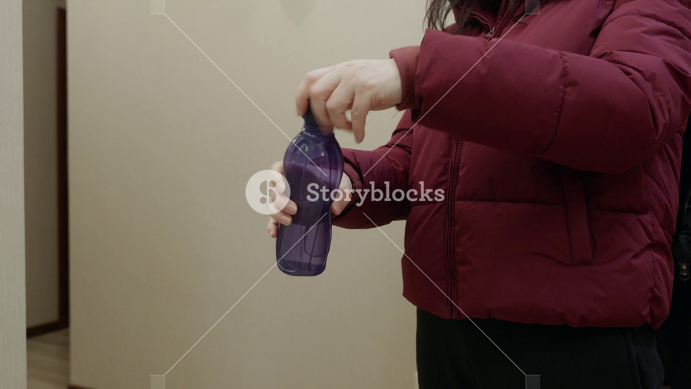 Adult woman holding purple reusable water bottle indoors, closing cap with hand. Healthy lifestyle, hydration and daily routine concept.