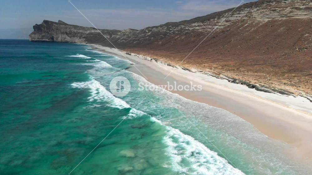 Flying over beautiful turquoise foamy waves of Indian ocean coming on a sandy beach near Salalah, Oman. Aerial shot, UHD