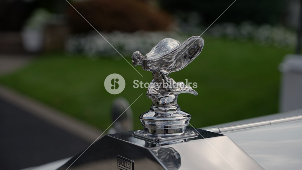 NEW YORK, USA - OCTOBER 7, 2025: Polished Chrome Hood Ornament CloseUp On Vintage Luxury Car, Shallow Depth Of Field, Blurred Garden