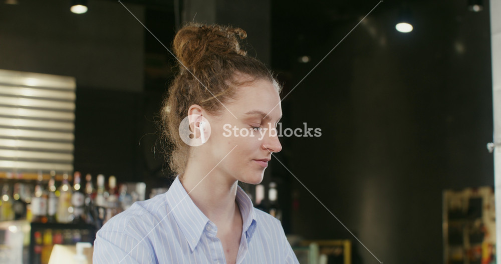 Young beautiful woman of European appearance, with curly hair gathered up, in wireless headphones starts video chat on a laptop, saying