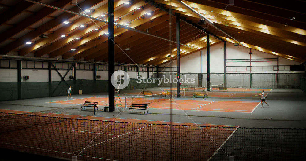 Young people - a man and a woman of European appearance are training to play tennis on one of the courts of a large indoor sports hall