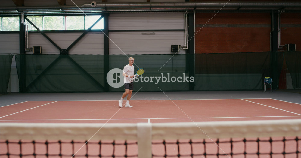 A young male tenessist of European appearance hits the last ball and wins the round. Playing professional tennis on the indoor tennis court