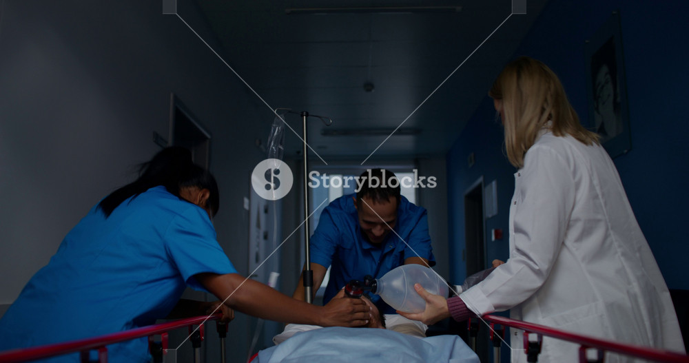 Medical workers carry a patient on a gurney along the hospital corridor. A woman holds an oxygen mask near his face