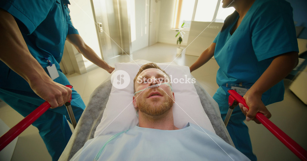 A man is lying on a medical gurney, he is being taken through the hospital corridor. The oxygen tube is in his nose