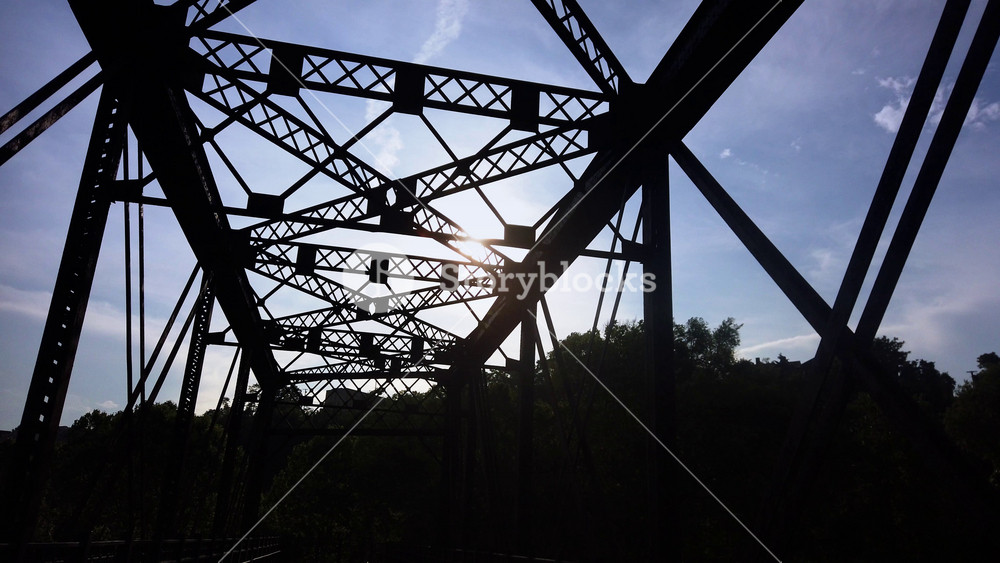 A view of sunlight shining through the steel beams of a bridge on the Three Rivers Heritage Trail on Washington's Landing in Pittsburgh, PA.