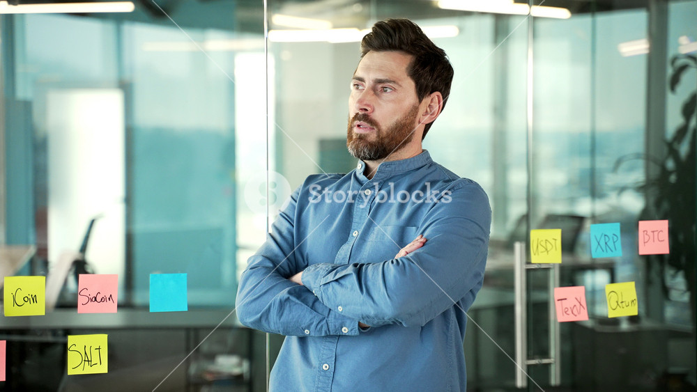 Portrait of a serious bearded businessman in shirt standing with crossed arms at the workplace in business office. Confident successful manager posing looking at camera. Head shot of handsome employee