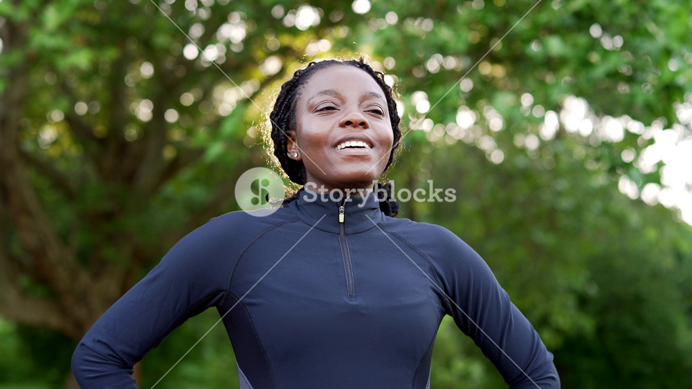 Refreshed african american sportswoman in tracksuit enjoys a quiet moment in an urban park. Close up as she breathes deeply with eyes closed, then opens them and smiles, feeling relaxed and renewed.