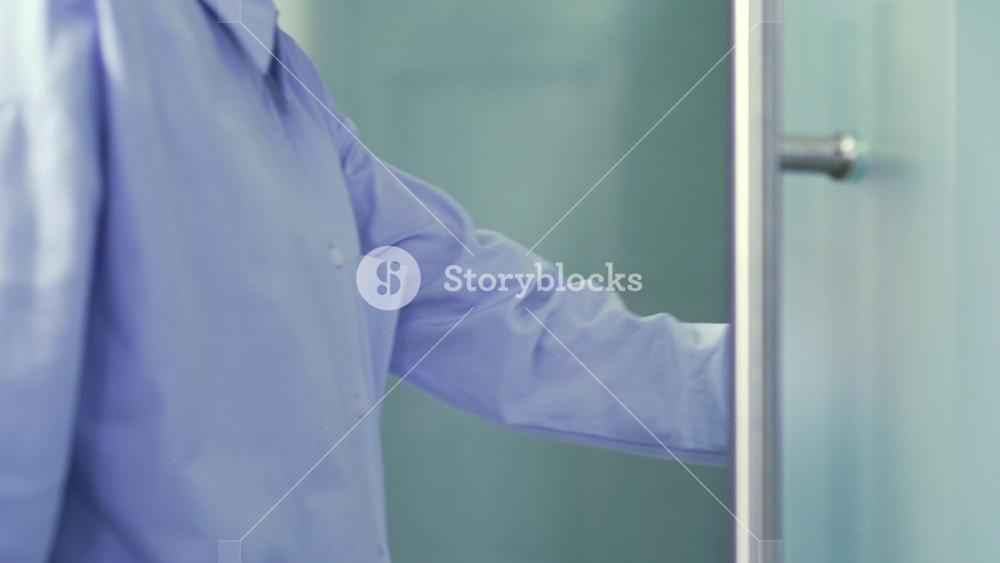 Close up of a female hand opening a glass office door holding a metal doorknob in a modern building. Businesswoman or employee in a shirt opens the door and enters the office to the workplace