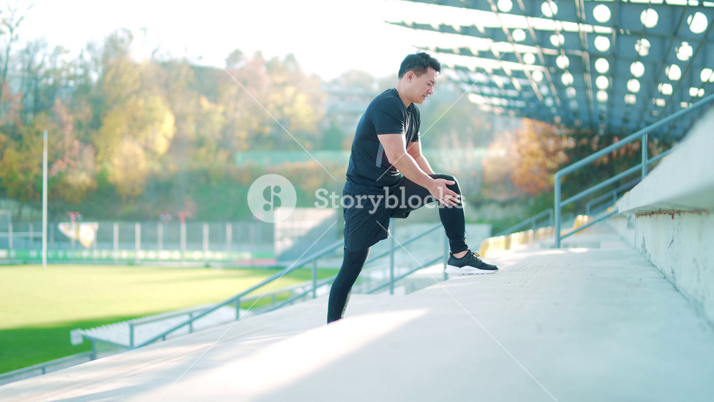 young asian runner athlete with muscle pain. Man massaging Stretching, trauma injury while jogging at the stadium outdoors. Fitness male sprain severe pain stretch pull. Leg muscle cramp calf sport