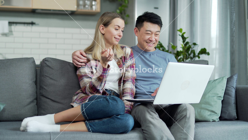 Happy young married couple shopping online choosing a product in online store together on laptop computer. Asian husband and wife browsing sitting on sofa at home. book a trip, travel tickets travel