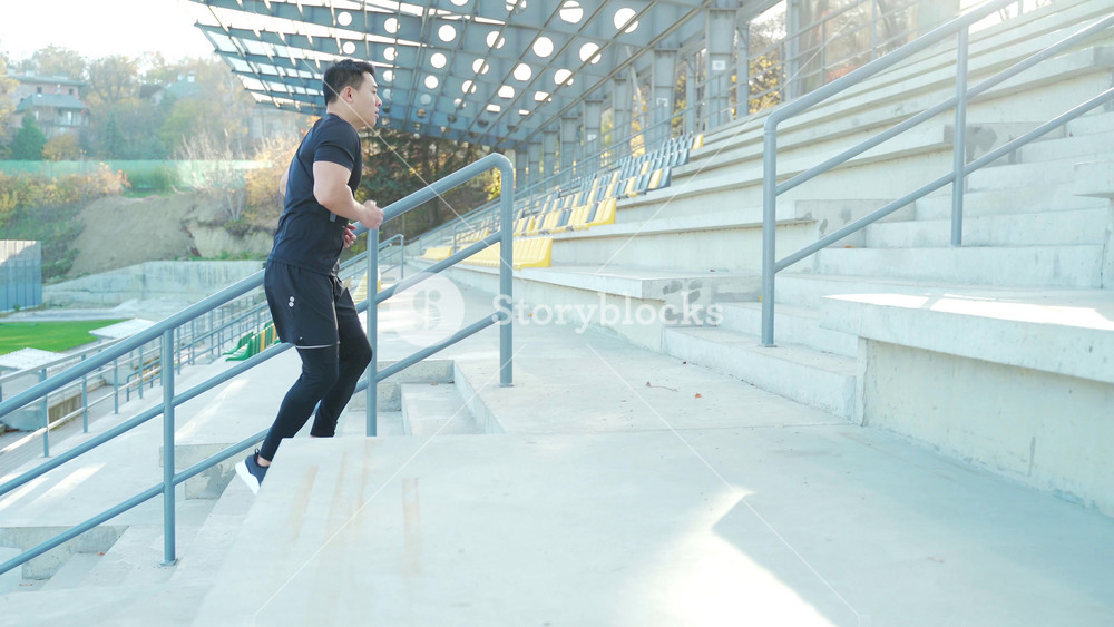 Asian male runner running around modern urban stadium up stairs Cardio morning jog climbing staircase man jogging Outdoor. sport man athlete workout in steps, in city. Active fitness healthy lifestyle