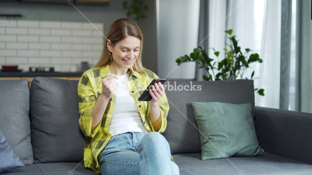 Amazed lucky woman extremely happy after read message in mobile phone at home Excited blond female looking at screen and pleased rejoices received great news on smartphone Moment of success triumph