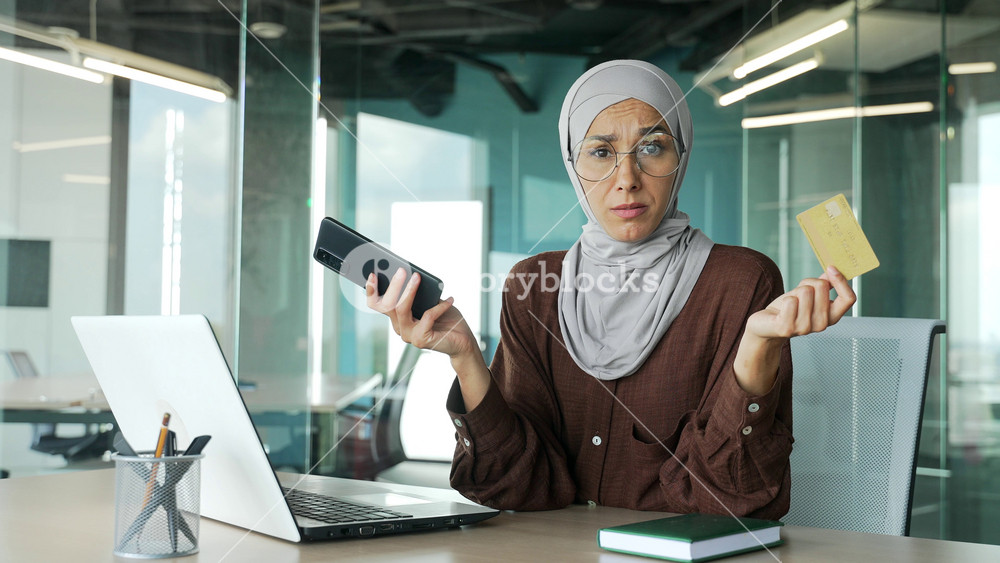 Stressed muslim businesswoman in hijab with credit card has problem with online order bad service blocked bank account failure with money transfer thoughtfully pondering on camera and shrugs at office
