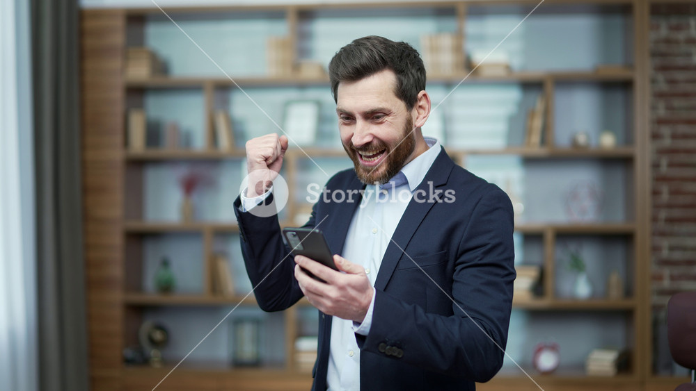 Overjoyed business man investor extremely happy after read message on smartphone at modern workplace Excited entrepreneur look at phone screen and pleased rejoices received great news at office indoor