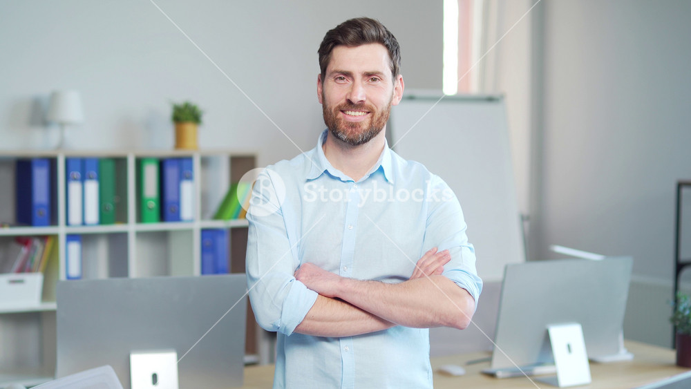 portrait of a handsome caucasian bearded office worker, employee of an entrepreneur who looks at the camera and smiles. Happy and cheerful male clerk at work. Businessman in a modern business office
