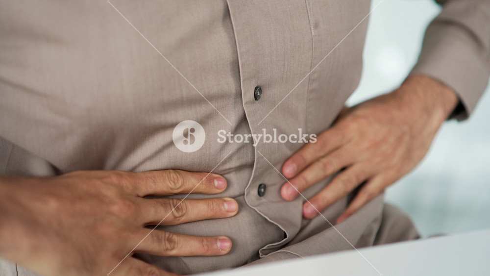 Close up. Male hands holding massaging stomach. Businessman in shirt feels stomach pain sitting at workplace in business office. Sick man suffers from bloating, gastritis poisoning, bloating or spasms