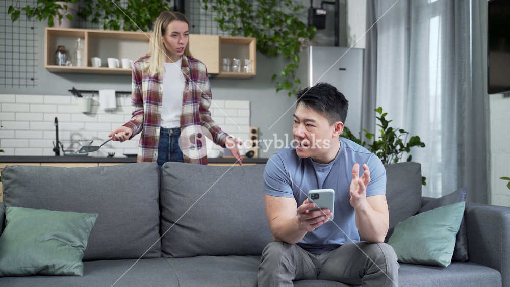 domestic violence woman quarreling with husband. Nervous asian man sitting on the couch in foreground while his wife shouting at him. couple problems and conflict in young family at home