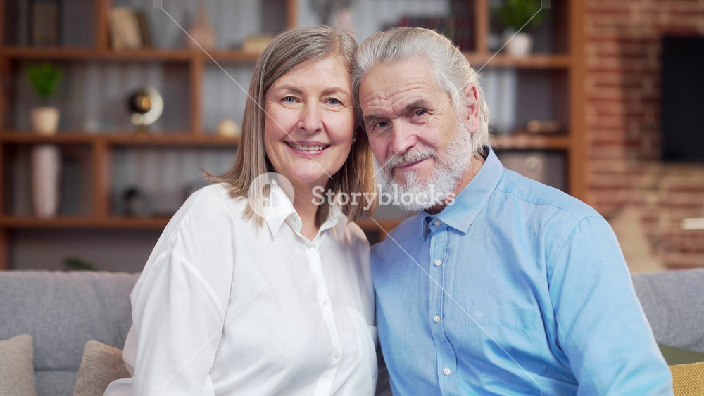 portrait of close up happy senior gray haired, married couple looking at camera while standing in room at home. Indoor. Husband and wife retirees smiling. Old people hug. Joyful grandparents bonding