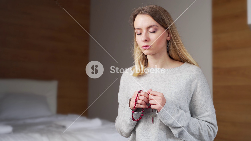 portrait young girl or woman sincerely praying on rosary at home. Prayer of repentance. Female believer with closed eyes and a beads in his hands. Christian or Orthodox Catholic in daily prayers