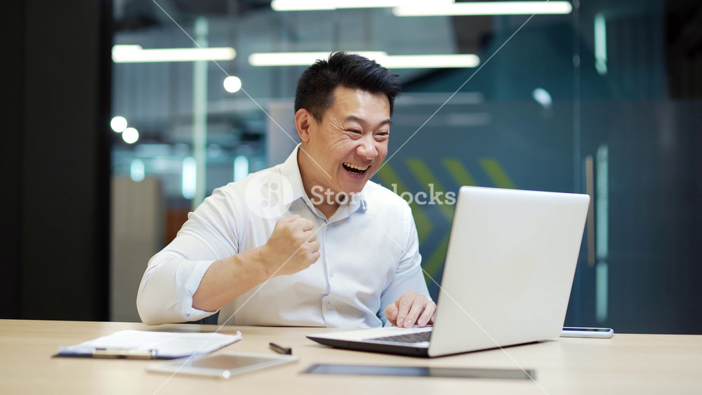 Happy Asian Business Man Employee Working on computer laptop Celebrates Successful YES Gesture. Working in office Stroke of Luck, won, Wins Big. worker victory good news result financial deal