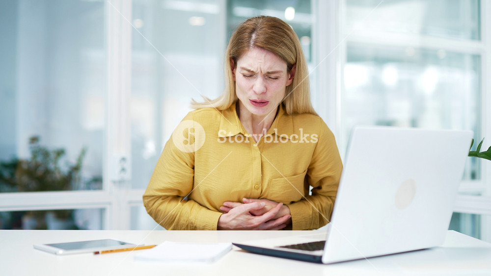 Disturbed busy mature business woman feeling gastritis or menstrual pain while working at modern office Sad female holding stomach with period indigestion overeating or poisoning at glass workplace