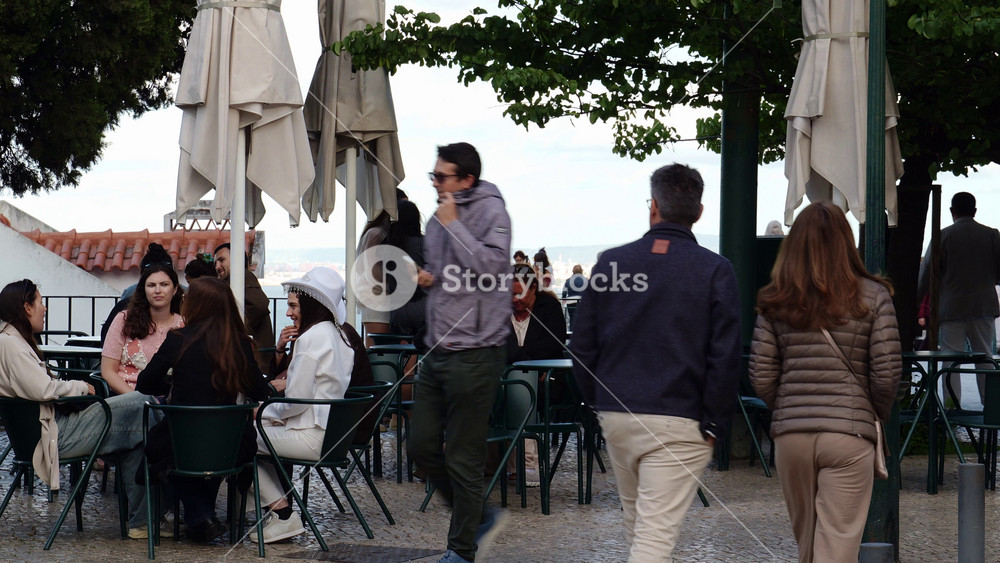 LISBON, PORTUGAL - MAY 15, 2026: Tourists and locals relaxing at tables under umbrellas at an outdoor cafe located at a scenic viewpoint, or